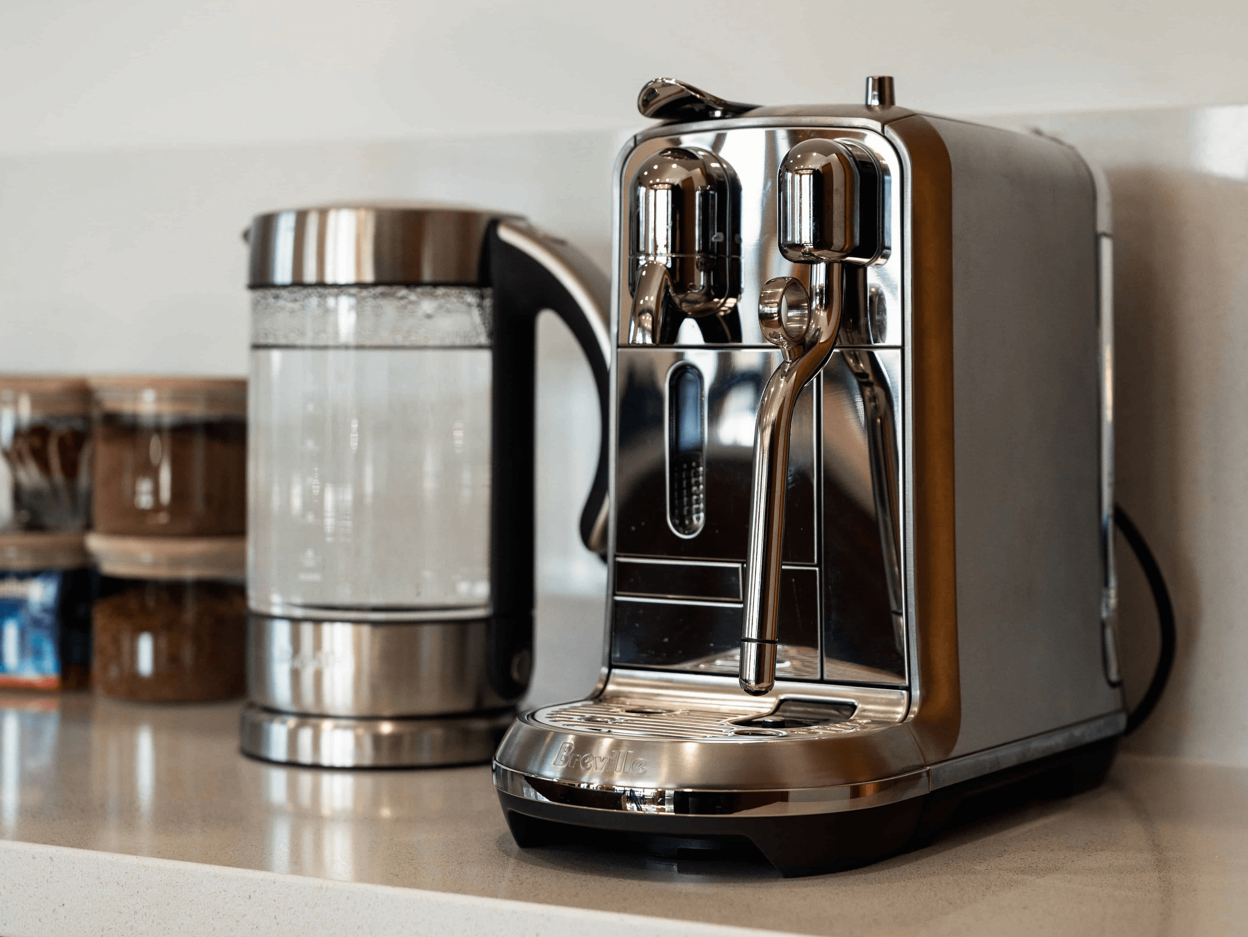 Stainless steel espresso machine next to an electric kettle with boiling water on a kitchen countertop.