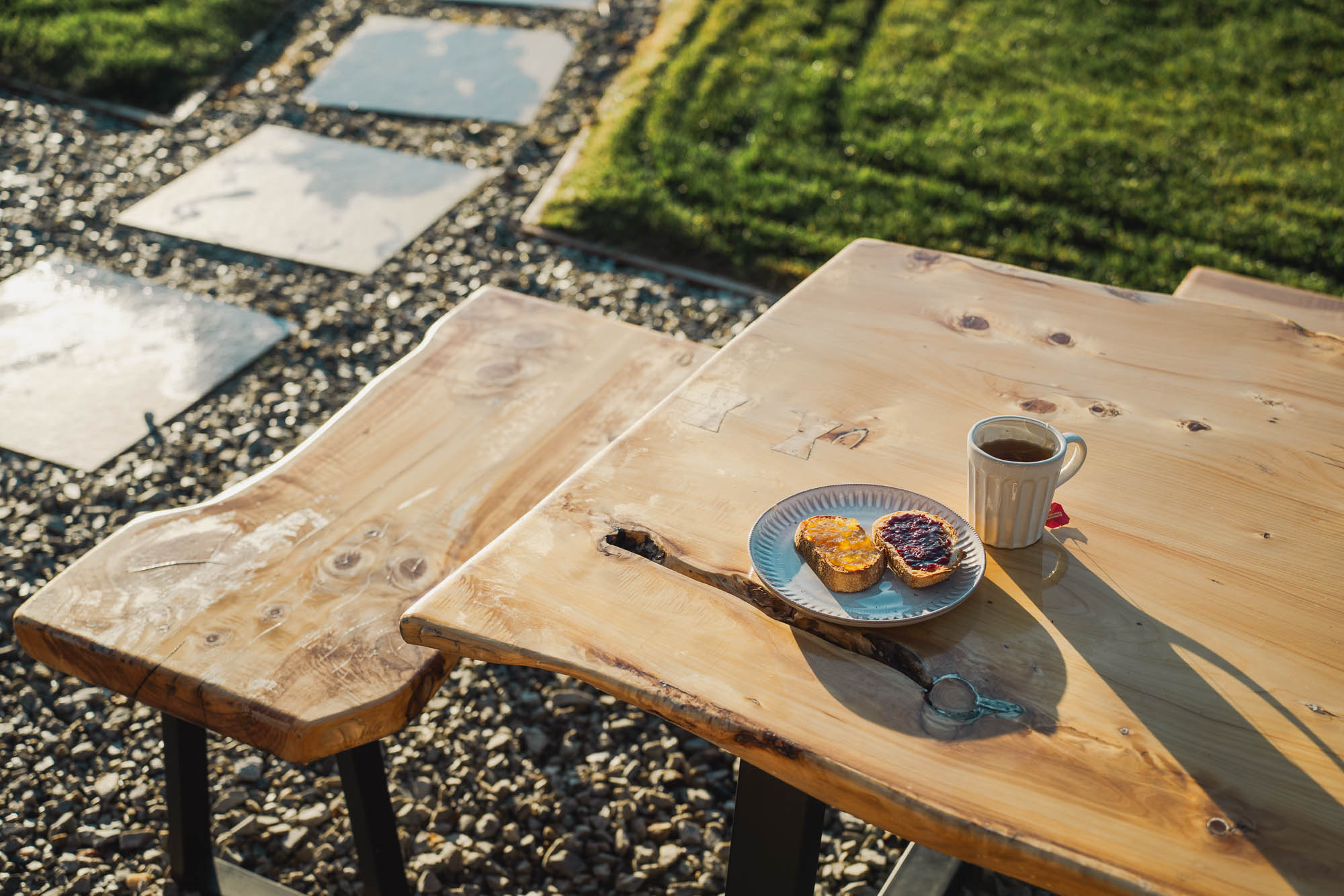 Wooden outdoor table and bench with a plate of two slices of bread with jam and a cup of tea.